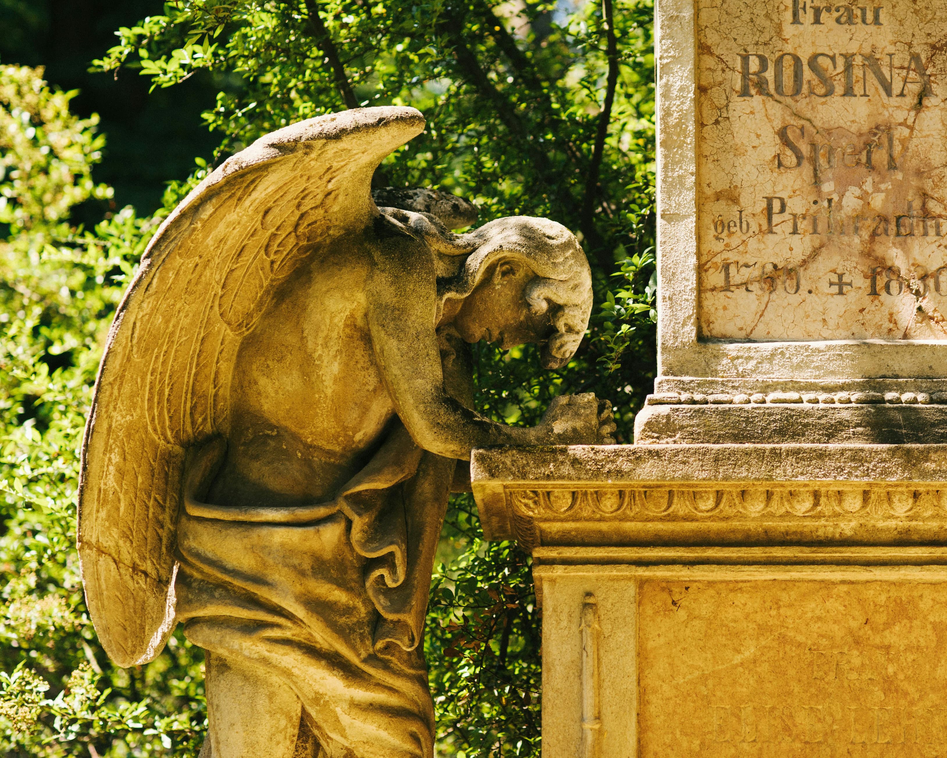 Steinerner Trauerengel mit gesenktem Kopf an einem alten Grabstein auf dem Ostfriedhof