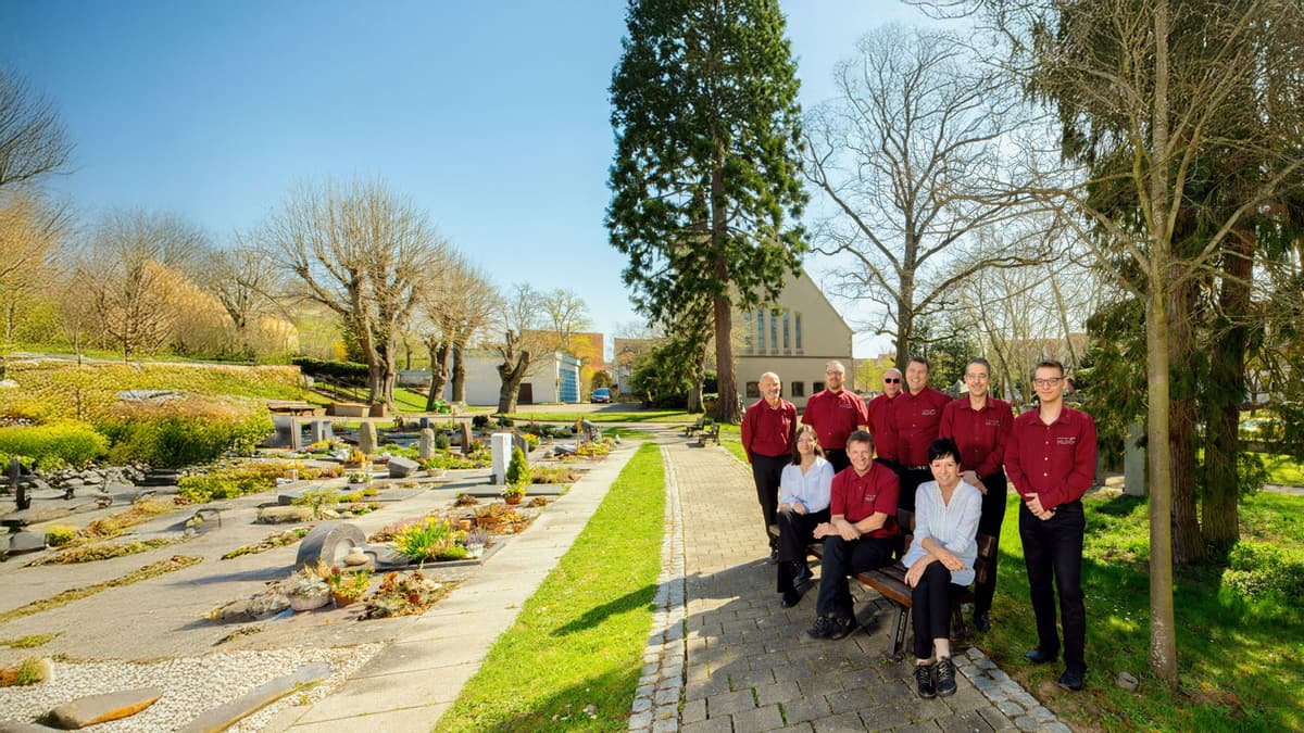 Team Kuhn Bestattungen am Friedhof Asperg Team von Kuhn Bestattungen in roter Kleidung auf einem Friedhof in Asperg bei sonnigem Wetter