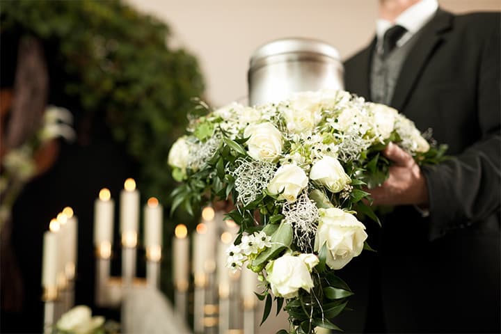 Urne mit weißem Blumenarrangement bei einer Trauerfeier auf dem Friedhof Pflugfelden, organisiert von Kuhn Bestattungen.