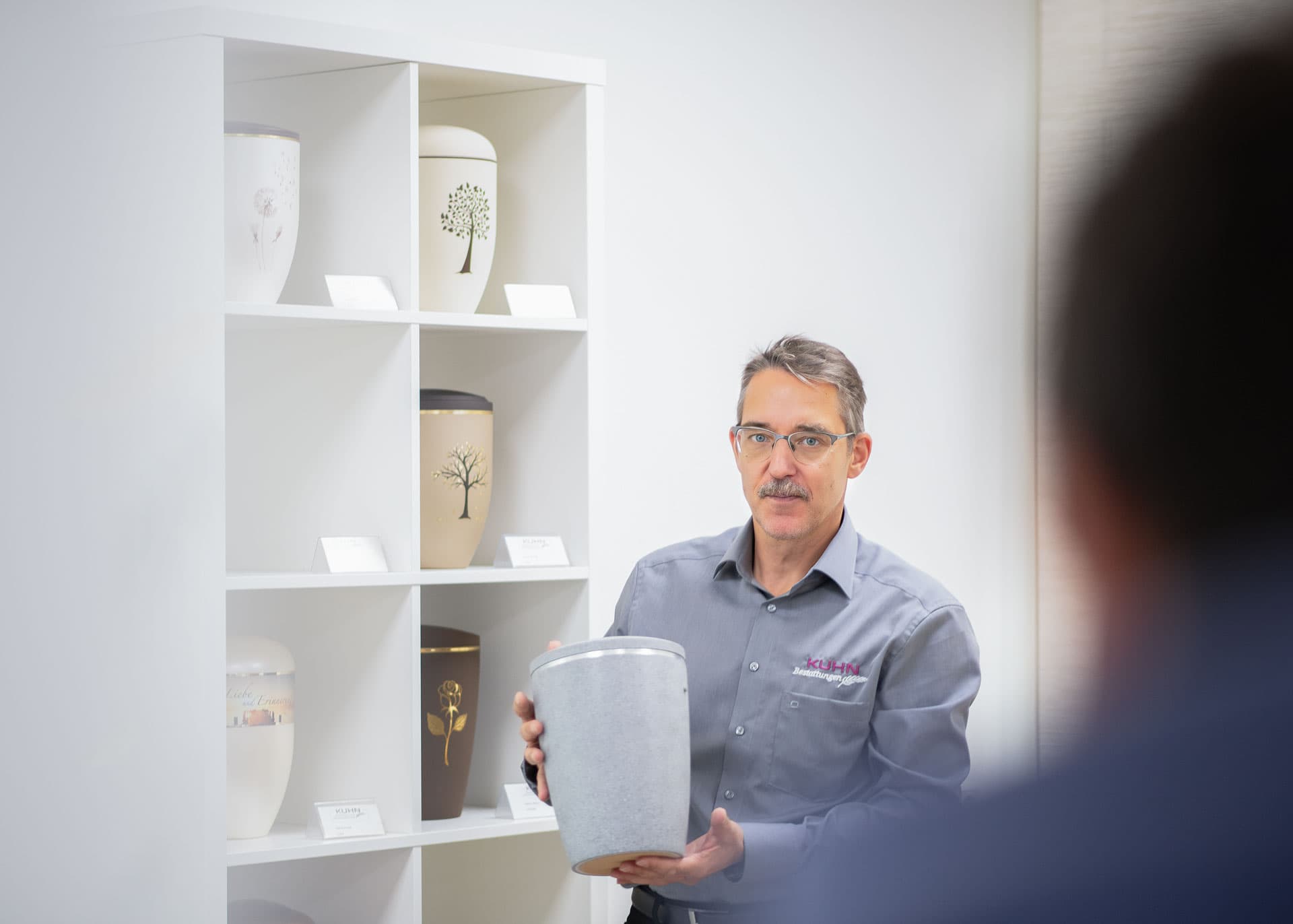 Urnenberatung – Kuhn Bestattungen Schwieberdingen Michael Groshaupt zeigt Urne in der Ausstellung von Kuhn Bestattungen am Standort Schwieberdingen
