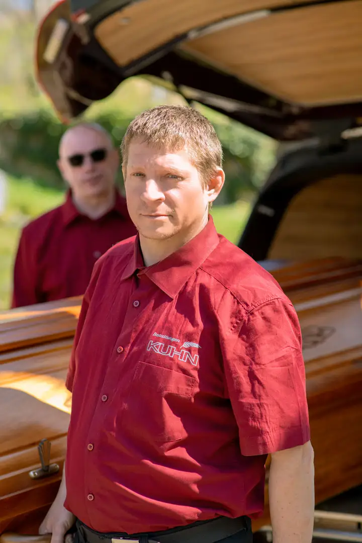 Unsere Mitarbeiter tragen Verantwortung mit Respekt und Mitgefühl Kuhn Bestattungen Mitarbeiter beim Sargtransport, Fokus auf Einzelperson im Vordergrund