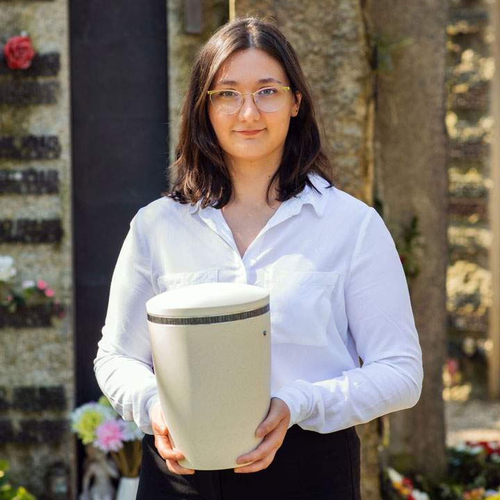 Einfühlsame Begleitung bei der Urnenbeisetzung in Asperg Junge Mitarbeiterin von Kuhn Bestattungen hält eine Urne am Friedhof in Asperg