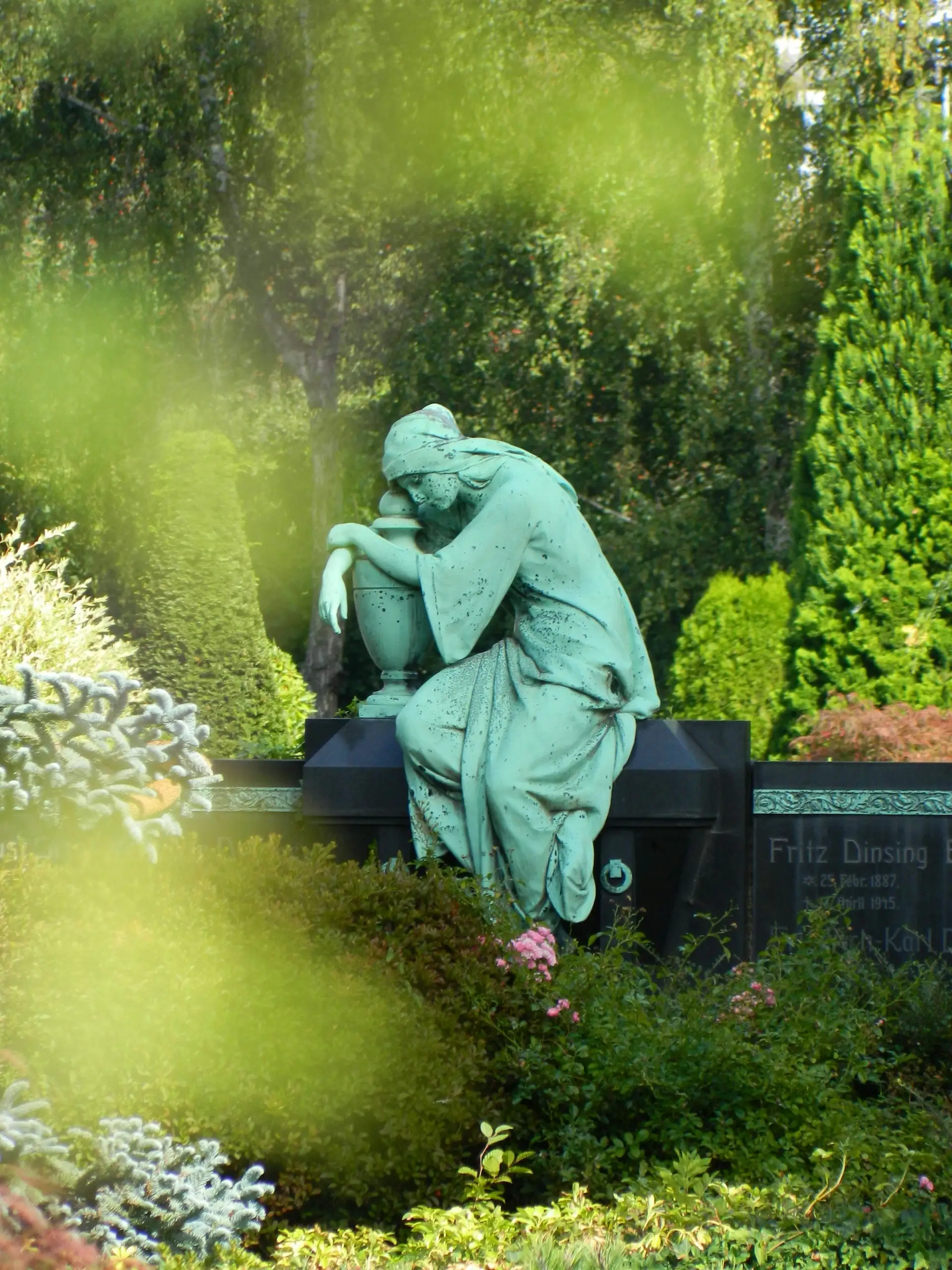 Bronzestatue einer trauernden Frau auf einem Friedhof Bronzestatue einer trauernden Frau auf einem historischen Grab inmitten grüner Bepflanzung.