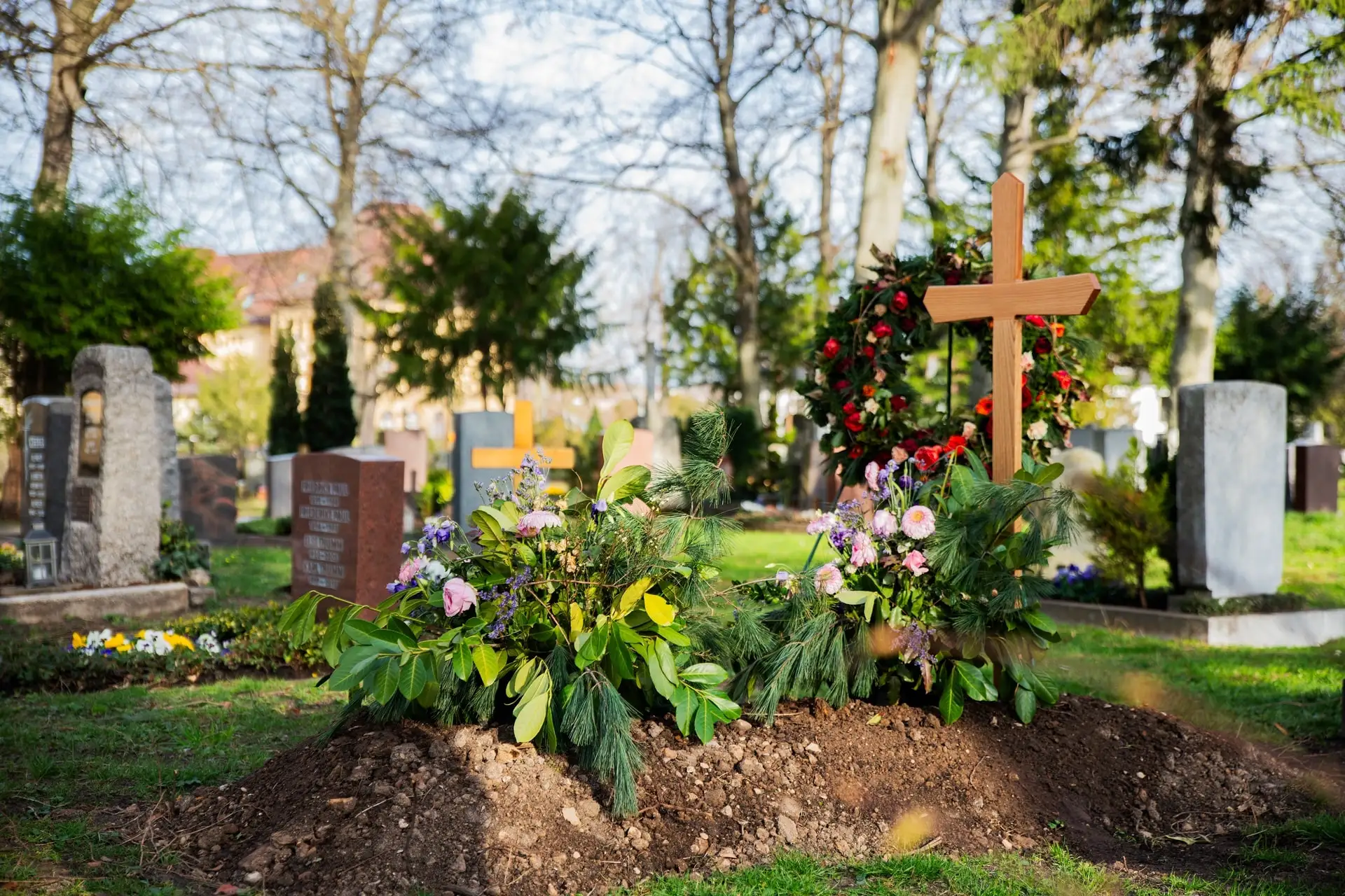 Frisch geschmücktes Grab Frisch geschmücktes Grab mit Blumenarrangement und Holzkreuz auf einem sonnigen Friedhof.